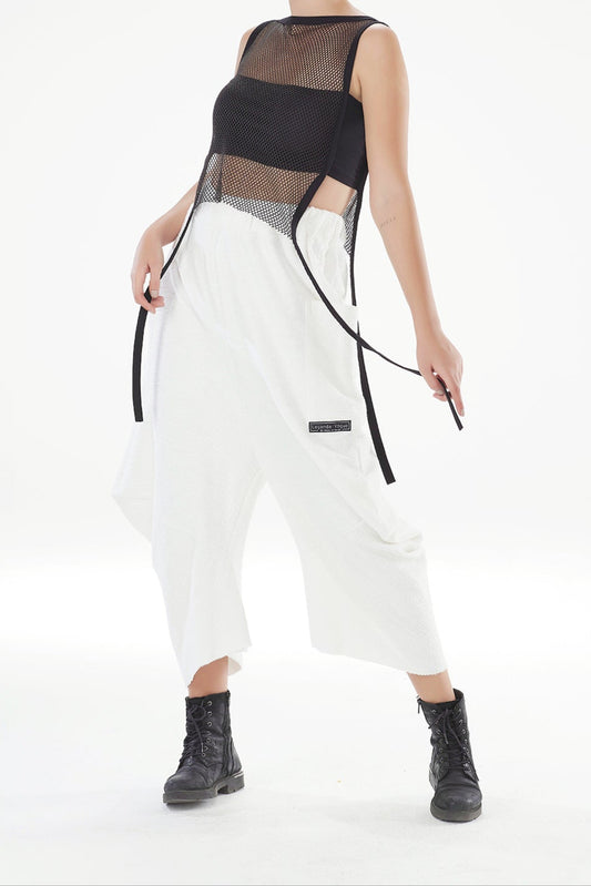 Model wearing a black sheer top and white pants with black boots on a white background