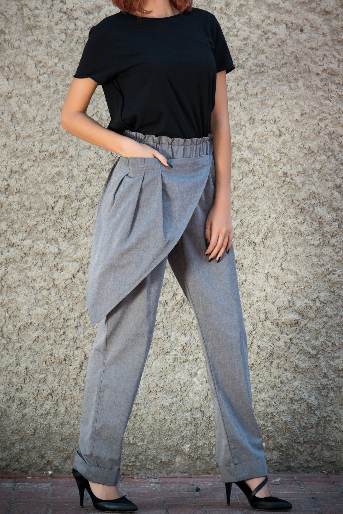 Woman wearing a black top and gray wide-leg pants against a textured wall.