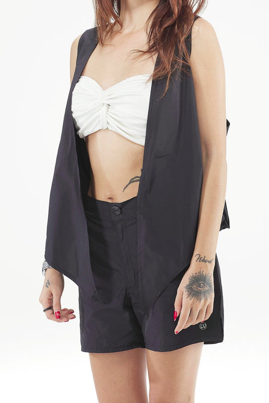 Woman wearing a black blazer over a white top and black shorts on a white background