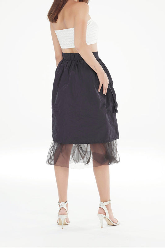Woman wearing a black skirt with sheer overlay and white top on a white background