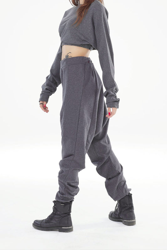 Woman wearing a gray outfit with a crop top and baggy pants on a white background