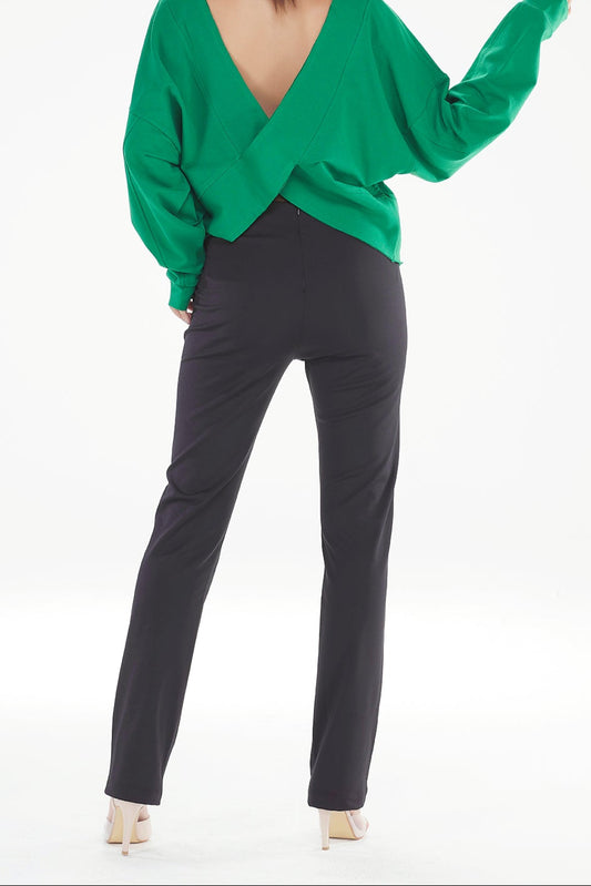 Person wearing a green open-back top and black pants on a white background