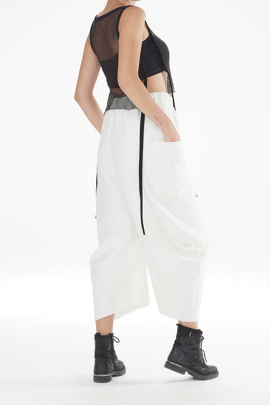 Woman wearing a black sleeveless top and white pants on a white background